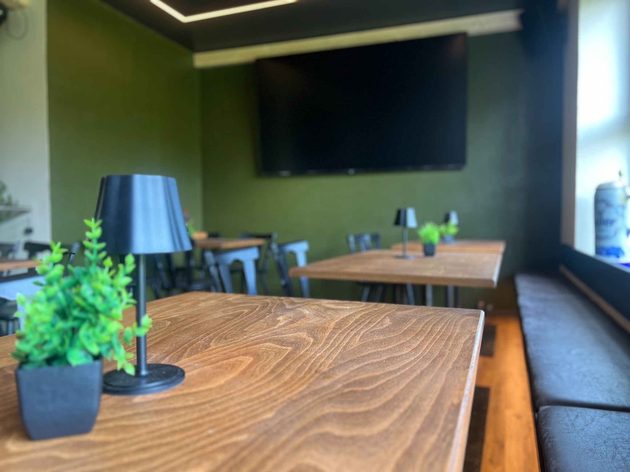 Blick in den TANKRAUM mit warmen Holztischen und dunkler grüner Wand